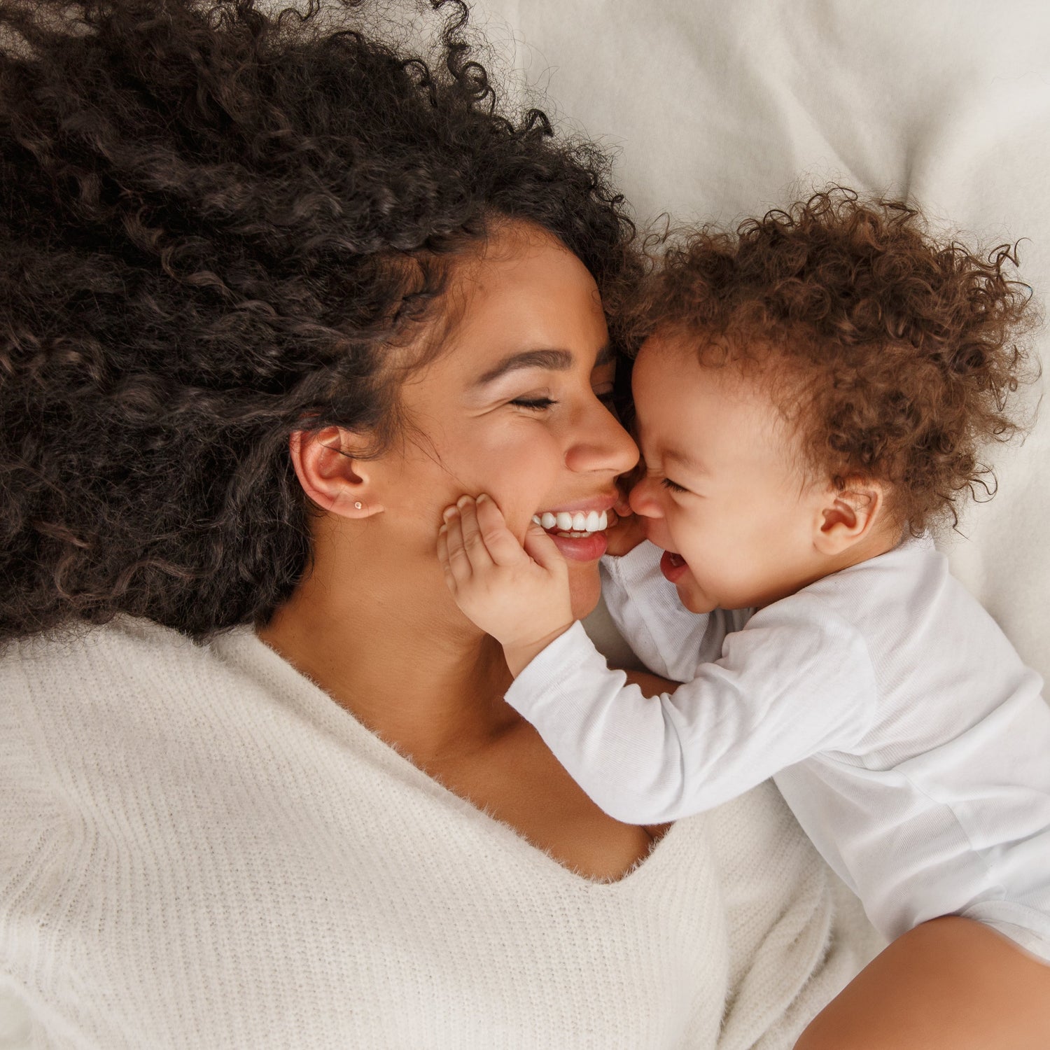 Woman and child lying on a white bed, smiling and laughing.